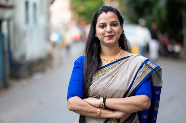 Outdoor waist up portrait of a beautiful Indian woman wearing sari with crossed arms and a smile on her face. She is standing near her car.
